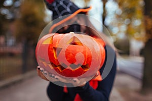 Halloween jack-o-lantern pumpkin. Scary girl holds carved pumpkin outdoors wearing mask against coronavirus. Close up