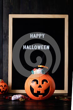 Halloween jack o lanterns pumpkins with sweets on black wooden background, blurred letter board with words Happy