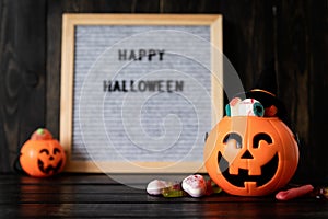 Halloween jack o lanterns pumpkins with sweets on black wooden background, blurred letter board with words Happy