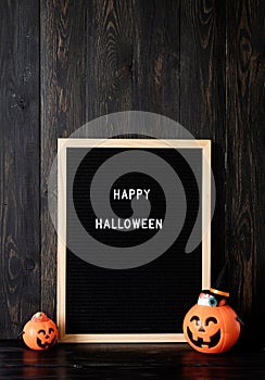 Halloween jack o lanterns pumpkins with sweets on black wooden background, letter board with words Happy Halloween