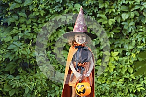 Halloween kids. funny cute happy little girl in orange witch costume, black hat with pumpkin Jack,