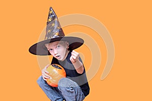 Halloween kids. Little Emotional boy in a wizard hat holding an orange pumpkin in his hands and showing a candy