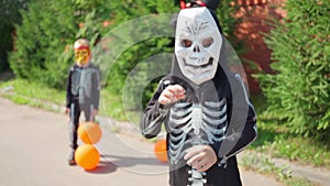 Halloween kids parade. Children in carnival costumes skeletons outdoors. Friends are having fun with orange balloons