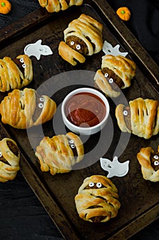 Halloween mummies - meatballs wrapped in dough with spicy tomato sauce on an old baking sheet.