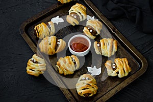 Halloween mummies - meatballs wrapped in dough with spicy tomato sauce on an old baking sheet.