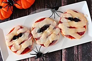 Halloween mummy mini pizzas on white plate over rustic wood