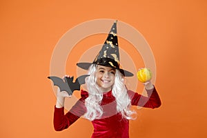 On Halloween night youre sure to have fright. Halloween girl in witch hat orange background. Little girl hold Halloween