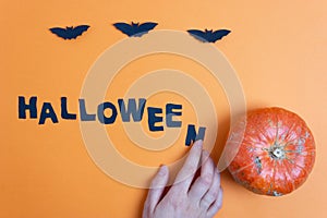 Halloween paper decorations and pumpkin on orange background, text halloween on the table. Trick or treat concept.