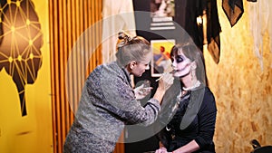 Halloween party, make-up artist draws a terrible makeup on the face of a brunette woman for a Halloween party. in the