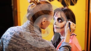 Halloween party, make-up artist draws a terrible makeup on the face of a brunette woman for a Halloween party. in the