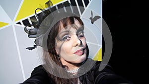 Halloween party, night, frightening portrait of a woman with a terrible makeup in a black witch suit, croaks in front of