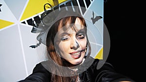 Halloween party, night, frightening portrait of a woman with a terrible makeup in a black witch suit, croaks in front of