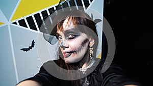Halloween party, night, frightening portrait of a woman with a terrible makeup in a black witch suit, croaks in front of