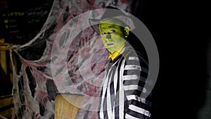 Halloween party, night, twilight, in the rays of light, a man with a terrible make-up, with a green face and a hat shows