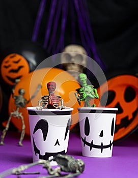 Halloween party. Skeletons coming out from the cup with balloons and skull in background