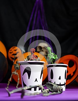 Halloween party. Skeletons coming out from the cup with balloons and skull in the background