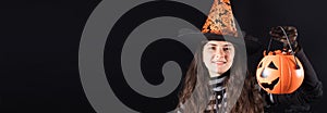 Halloween people banner. A woman in a witch costume on a black background holds bucket pumpkin with candy and smile