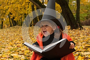 A Halloween photo of a little girl representing a wicked witch dressed in black and orange and holding a magic book