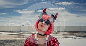 Halloween. Portrait of a beautiful girl in a red wig with horns close-up against a blue sky. Sitting on the foof. Red