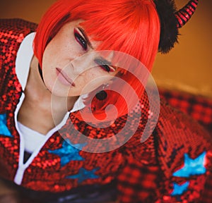 Halloween. Portrait of a beautiful girl in a red wig with horns closeup. Red, festive makeup.