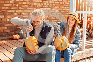 Halloween Preparaton Concept. Young couple outdoors making jack-o`-lantern carving pumpkins smiling concentrated