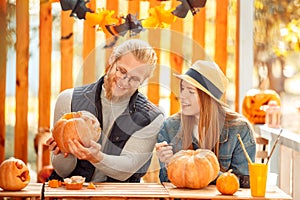 Halloween Preparaton Concept. Young couple sitting at table outdoors man showing jack-o`-lantern to woman happy