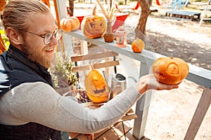 Halloween Preparaton Concept. Young man in glasses decorating house with jack-o`-lantern holding pumpkin smiling