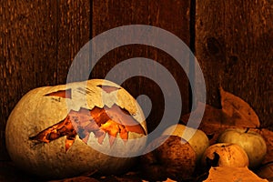 Halloween pumpkin and apples on autumn leaves next to a wooden background.