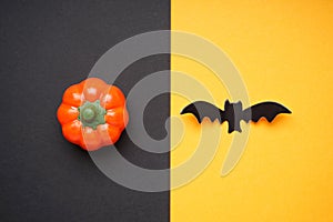 Halloween pumpkin and bat on black-yellow background, flat lay. Halloween concept