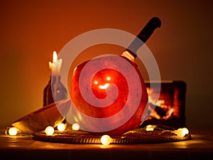 Halloween pumpkin with a comically carved face sits on a table, atmosphere is enhanced by warm burning candle and