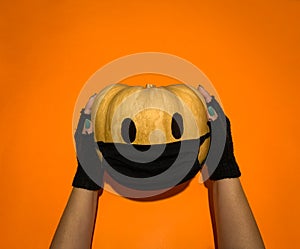 Halloween pumpkin covered with face mask against coronavirus holded by hands