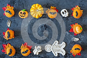 Halloween pumpkin cupcakes frame with scary symbols served on black background