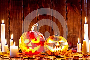 Halloween pumpkin with glowing face on a wooden background with many flaming candles and autumn leaves. Idea for flyers, poster, p