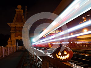 Halloween pumpkin with a glowing grimace at night on the railway bridge. In the background there are rails and blurry