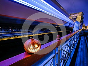Halloween pumpkin with a glowing grimace at night on the railway bridge. In the background there are rails and blurry