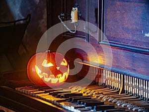 Halloween pumpkin lantern with scary face glowing inside. Decoration. Old piano. Gothic concept.