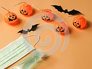 Halloween pumpkin lights , black paper bats,medical mask and alcohol sanitizer gel on orange background. Halloween , COVID-19