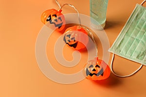 Halloween pumpkin lights, medical mask and alcohol sanitizer gel on orange background. Halloween , COVID-19 prevention and new