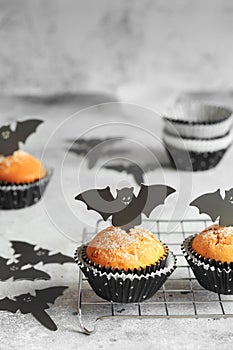 Halloween pumpkin muffins in black capsules decorated with cardboard bats. Festive Halloween cupcakes. Close-up view of delicious