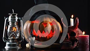 Halloween. Pumpkin, skull, oil lamp, candle, witch standing on table.