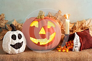 Halloween Pumpkin Still Life Scene with ghost gour, candle, and treats bag, all on a burlap table with fall leaves and textured bl