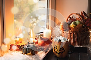 Halloween with pumpkins, coffee with marshmallow on windowsill. Stay at home in lockdown. Cozy still-life, furskin, garland