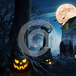 Halloween pumpkins near a tree in a cemetery with a scary house. Halloween background at night forest with moon and bats