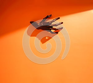 Halloween scary background. Dark monster hand reaching through orange paper wall.