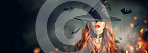 Halloween. witch portrait. Beautiful young woman in witches hat with long curly red hair over spooky dark magic forest