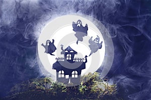 Halloween. Silhouette of an old house on a background of the full moon. Silhouettes of ghosts, fog