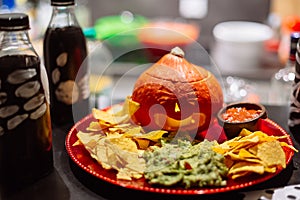 Halloween snack party plate with carved pumpkin, nachos, guacamole and salsa dip