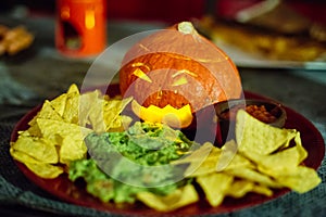 Halloween snack party plate with carved pumpkin, nachos, guacamole and salsa dip