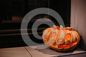 Halloween street decor with spooky Jack-o`-lantern. Pumpkin with scary carved glowing face and candle light in dark, modern