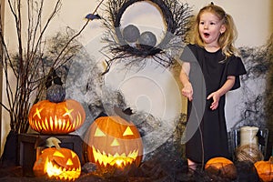 Halloween surprised blonde little witch girl with magic wand. Pumpkins cobwebs.